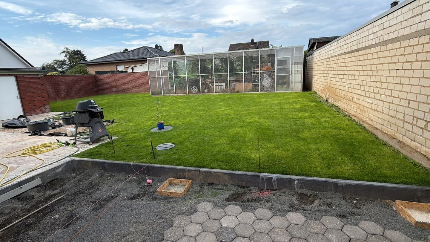 Rasen und eine angrenzende gepflasterte Fläche in einem Hausgarten
