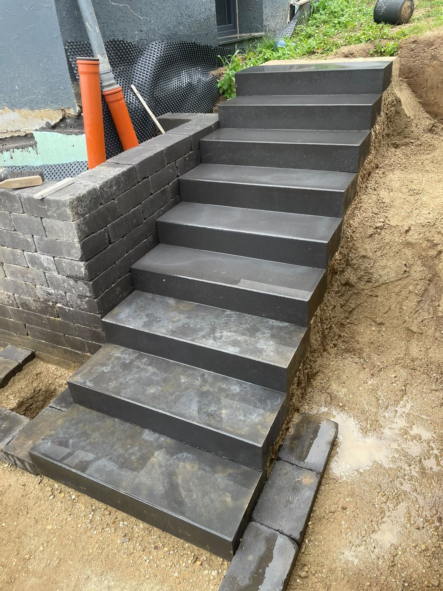 Treppe aus dunklen Betonblockstufen mit Stützmauer in einem Hang